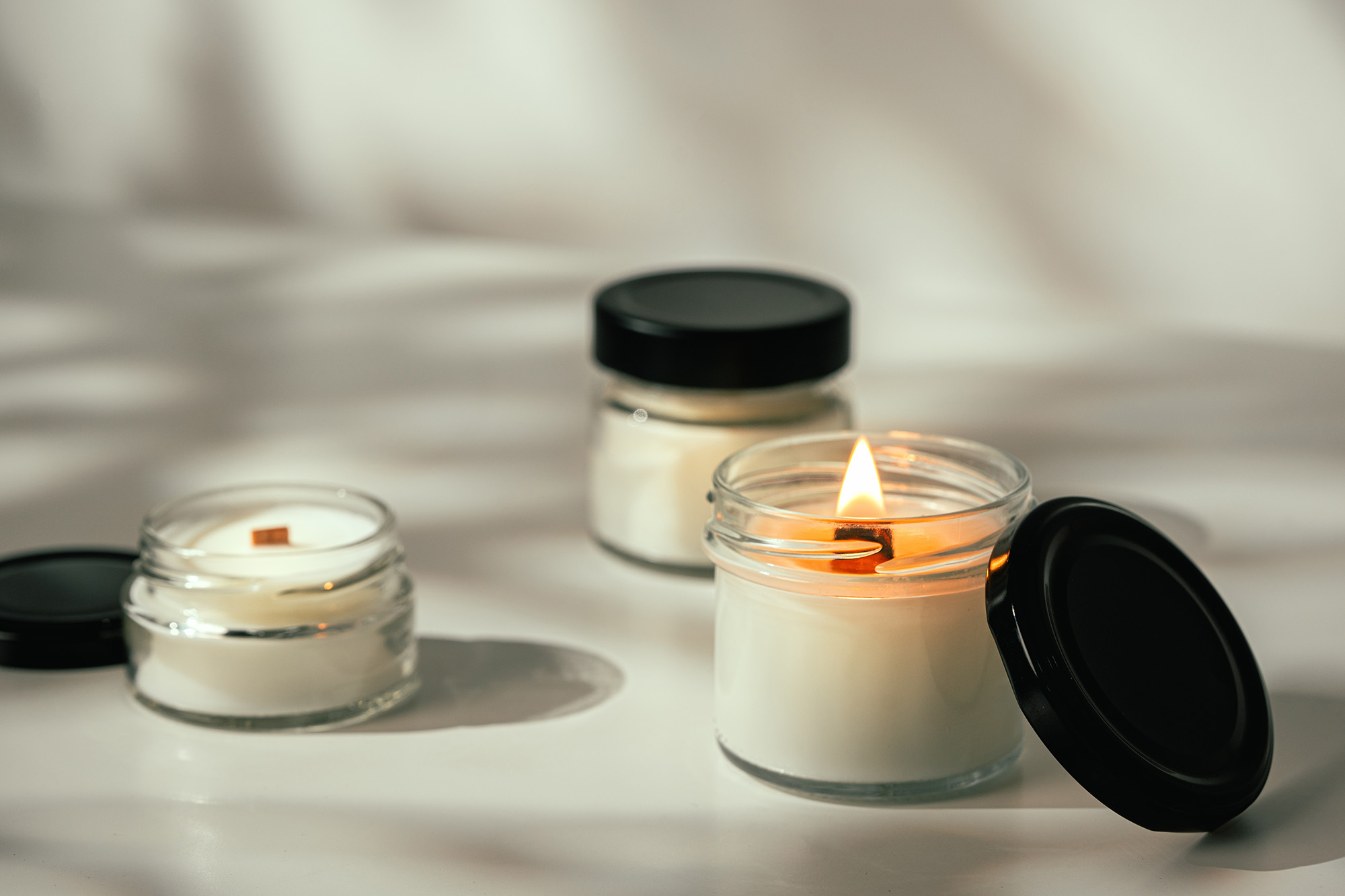 Lit Glass Jar Candles on White Surface With Grey Background